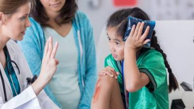 Young female soccer athlete is dazed while ER doctor asks her questions. The girl has an icepack on her head. The girl's mom is in the background.