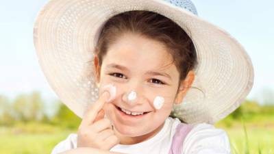 Beautiful little girl applying sun cream to her face