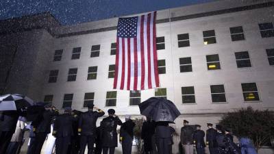 Supervivientes y miembros del Ejército escuchan el himno nacional junto a una bandera desplegada en el Pentágono, en Arlington, Virginia, Estados Unidos este domingo durante el 21º aniversario del atentado a las Torres Gemelas y el Pentágono del 11-S.