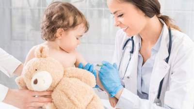 Young woman pediatrician performs a vaccination of a little girl. The girl is holding a mascot.