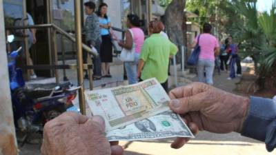 Un señor muestra un peso cubano y un dólar afuera de un centro de cambio.
