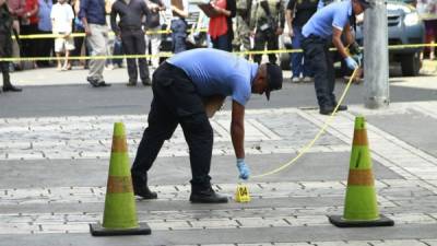 Agentes de inspecciones oculares recogen pruebas del asesinato del cambista Nixon Alvarado en el parque central de San Pedro Sula.
