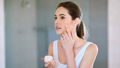 An attractive young woman applying cream to her face