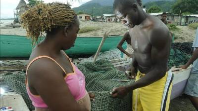 Fotografía de archivo del 20 de agosto de 2011, de una pareja de Garifunas (negros) reparando una red de pescar en la comunidad de Sambo Creek en el caribe hondureño. EFE/Archivo
