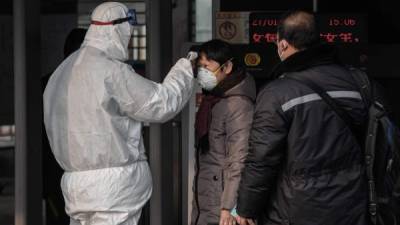 Security personnel wearing protective clothing to help stop the spread of a deadly virus which began in Wuhan, checks the temperature of a woman at a subway station entrance in Beijing on January 27, 2020. - China on January 27 extended its biggest national holiday to buy time in the fight against a viral epidemic and neighbouring Mongolia closed its border, after the death toll spiked to 81 despite unprecedented quarantine measures. (Photo by NICOLAS ASFOURI / AFP)