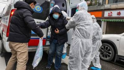This photo taken on January 26, 2020 shows a patient assisted by medical staff members wearing protective clothing to help stop the spread of a deadly virus which began in the city, as he gets off an ambulance in Wuhan in China's central Hubei province. - China on January 27 extended its biggest national holiday to buy time in the fight against a viral epidemic, as the death toll spiked to 81 despite unprecedented quarantine measures and travel lockdowns. (Photo by STR / AFP) / China OUT