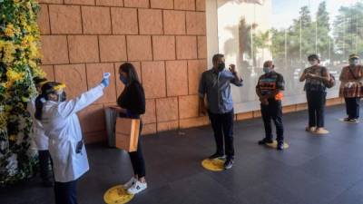 Una mujer controla la temperatura corporal de un consumidor en un centro comercial en el barrio de Polanco, en la Ciudad de México. AFP