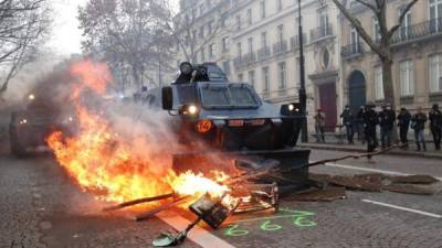 Vehículos blindados tratan de despejar una barricada en llamas en las inmediaciones de los Campos Eliseos de París, durante las protestas convocadas por los chalecos amarillos este sábado en París. EFE