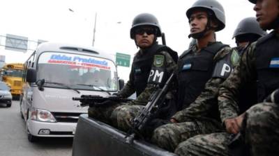 Varios policías militares patrullan una calle en Honduras, al fondo se observa un microbús del transporte público.