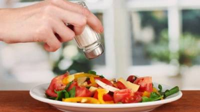 Hand adding salt using salt shaker on bright backgroundHand adding salt isolated on white