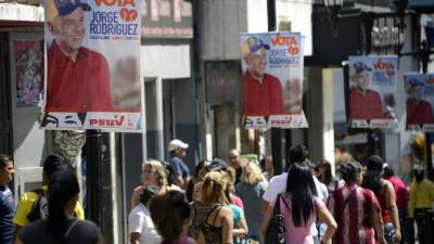 Deceneas de personas caminan por las calles de Cararas, donde se observan diferentes afiches de los candidatos a las elecciones municipales.