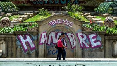 Una pareja camina por graffitis que dice 'We Are Hungry' y 'Maduro Dictator' en Caracas el 8 de agosto de 2017. AFP
