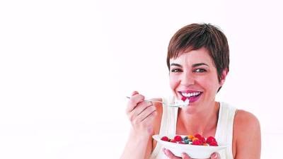 Young woman smiling and eating a bowl of fruit. Horizontal shot.