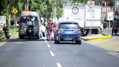 Dos niñas asoman sus caras en las ventanas de los carros para que los conductores les den el dinero que las madres esperan sentadas en una acera.