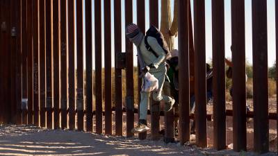 Migrantes cruzan el muro entre la frontera de México y Arizona.