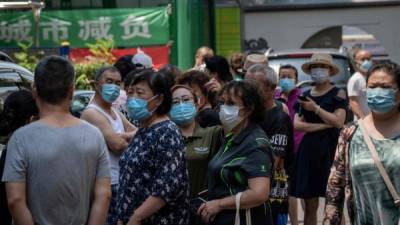 Residentes esperan detrás de una puerta de entrada para ser transportados a través de un autobús provisto a un sitio para la prueba del coronavirus COVID-19 en Beijing. AFP
