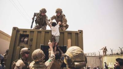 In this image courtesy of the US Central Command Public Affairs, British and Turkish coalition forces, and US Marines assist a child during an evacuation at Hamid Karzai International Airport in Kabul on August 20, 2021. - A Pentagon official confirmed Friday that US evacuation operations from Kabul's airport have been stalling because the receiving base in Qatar is overflowing and could not receive evacuees. 'There has been a considerable amount of time today where there haven't been departures,' Brigadier General Dan DeVoe of the US Air Mobility Command told reporters. (Photo by Victor MANCILLA / US Central Command Public Affairs / AFP) / RESTRICTED TO EDITORIAL USE - MANDATORY CREDIT 'AFP PHOTO / US Marine Corps / Staff Sgt. Victor Mancilla' - NO MARKETING - NO ADVERTISING CAMPAIGNS - DISTRIBUTED AS A SERVICE TO CLIENTS