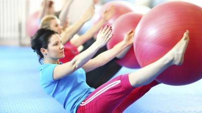 Small group of adult caucasian women doing pilates.Sitting on the floor and holding their legs up with red Pilates ball between. Trying to reach the ball with their arms. This is excellent abs exercise.Focus on the closest person.