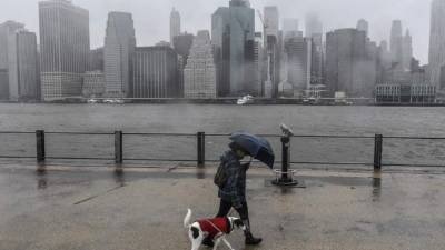 Una persona pasea con su mascota con los rascacielos de la ciudad de Nueva York en la distancia. Fuertes vientos y lluvia han azotado la región en las últimas horas.