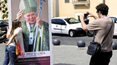 Tourists take pictures with a placard showing a picture of late pope John Paul II exhibited in front of the Pontifical gregorian University in Rome on April 20, 2011. The Vatican said late pope John Paul II's coffin will lie in state after his beatification on May 1. AFP PHOTO / VINCENZO PINTO