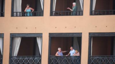 Tourists stand on the balcony of their rooms at the H10 Costa Adeje Palace Hotel in La Caleta, on February 25, 2020, where hundreds of people were confined to their rooms after an Italian tourist was hospitalised with a suspected case of coronavirus. - Tourists staying in a four-star hotel on the Spanish island of Tenerife, in the Canary archipielago, were confined to their rooms today following the announcement of a suspected novel coronavirus, COVID-19, case waiting for official confirmation. This possible case was detected yesterday in Tenerife, where an Italian national passed a first test which turned out to be positive, announced the Spanish Ministry of Health. (Photo by DESIREE MARTIN / AFP)