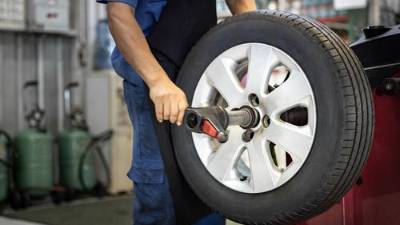 Mecánico de automóviles utiliza una máquina balanceadora de neumáticos y hace girar los neumáticos. Alineación de ruedas por computadora.