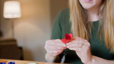 A young adult woman creates a paper rose.