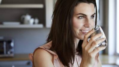 Beautiful woman drinking water and smiling in kitchen