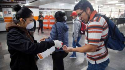 Un empleado desinfecta las manos del hombre en una estación de metro en la Ciudad de México. AFP
