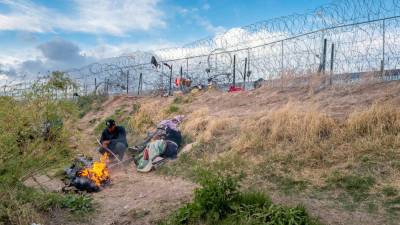 Una familia de migrantes espera frente a la cerca levantada por la Guardia Nacional de Texas para poder ingresar a EEUU.