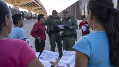 (FILES) In this file photo taken on May 16, 2019 US Customs and Border Protection agents check documents of a small group of migrants, who crossed the Rio Grande from Juarez, Mexico in El Paso, Texas. - A federal judge in California on July 24, 2019, issued a preliminary injunction blocking the Trump administration's new rule barring most immigrants from obtaining asylum in the US if they transit through Mexico. (Photo by Paul Ratje / AFP)