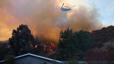 Un helicóptero arroja agua sobre una casa durante el incendio forestal de Palisades en Los Ángeles, California (EEUU).