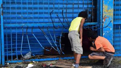 Niños curiosos se asoman pro un agujero creado por saqueadores en un negocio de abarrotes.