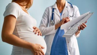 Pregnant female looking at paper with medical prescriptions held by her therapeutist