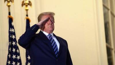 TOPSHOT - US President Donald Trump salutes from the Truman Balcony upon his return to the White House from Walter Reed Medical Center, where he underwent treatment for Covid-19, in Washington, DC, on October 5, 2020. (Photo by NICHOLAS KAMM / AFP)