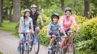 A family of four is going on a bike ride together through the park on a beautiful sunny day.