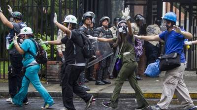 Un grupo de paramédicos voluntarios caminan con sus manos en alto en medio de los intentos de la Policía Nacional Bolivariana (GNB) por dispersar un grupo de manifestantes opositores el jueves.
