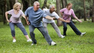 Multi-ethnic group of adults practicing tai chi in park. Main focus on senior man (60s) in blue shirt.