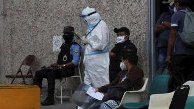 Una doctora pasa cerca de personas que tienen familiares sospechosos de coronavirus en centro de triaje del Hospital Escuela Universitario, hoy sábado en Tegucigalpa (Honduras). EFE/Gustavo Amador