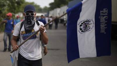 Un hombre sostiene una bandera de El Salvador durante la llegada de un grupo de más de 500 migrantes salvadoreños a la frontera de Ahuachapán (El Salvador) para ingresar a territorio guatemalteco y continuar su ruta hacia la nación norteamericana. EFE
