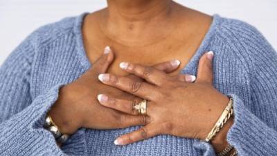 Senior African descent woman clutches chest in pain.