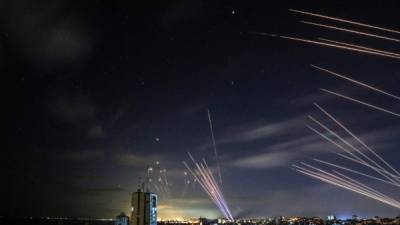 En el fondo, el sistema israelí de defensa de misiles Domo de Hierro intercepta cohetes disparados por el movimiento Hamás hacia el sur de Israel desde Beit Lahia en el norte de la Franja de Gaza, y en primer plano decenas de otros cohetes intercepta (RR) disparados por Hampas mientras la Cúpula de Hierro está ocupada con los primeros cohetes, como se ve en el cielo sobre la Franja de Gaza durante la noche del 16 de mayo de 2021.