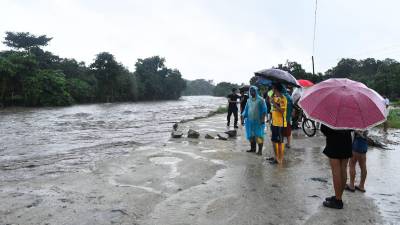 Sampedranos se cubren de la lluvia con paraguas, mientras observan la crecida de un río.