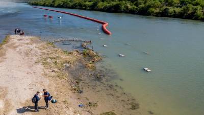 Un grupo de migrantes se prepara para cruzar el río Bravo frente a una barrera de boyas colocadas por orden del gobernador Abbott.