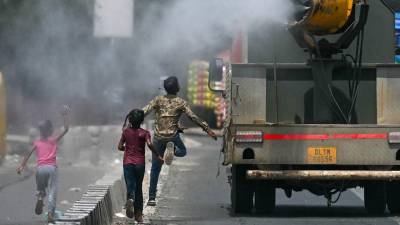 Un grupo de niños corren detrás de un auto que rocía agua en medio de una ola de calor en la India.