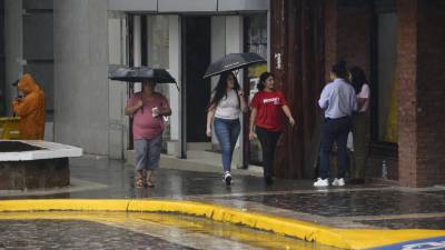 Tres mujeres caminan bajo la lluvia en el centro de San Pedro Sula.