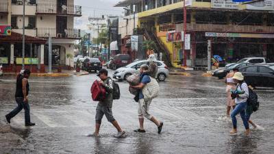 Personas caminan por una calle encharcada debido a las fuertes lluvias en el balneario de Acapulco, estado de Guerrero (México).