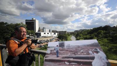 El fotoperiodista hondureño Estalin Irías muestra una fotografía, el 23 de octubre de 2023, en el lugar donde la tomo hace 25 años, de una niña que se dirige a la iglesia a su primera comunión y camina por el puente El Chile de Tegucigalpa, donde se observa el daño causado por el paso del mortal huracán Mitch, Tegucigalpa (Honduras).