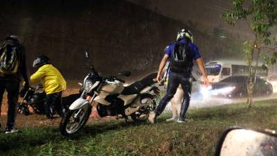 Hondureños intentan avanzar con motocicletas y automóviles por una calle inundada por la lluvia en Tegucigalpa.