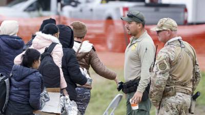 Fotografía de archivo donde se ve a un grupo de migrantes pasar frente a un agente de la Patrulla Fronteriza y una Guardia Nacional de Texas en Shelby Park en Eagle Pass, Texas, Estados Unidos.